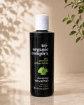 A bottle of Chromastatics Tri-Organic Complex Clarifying Shampoo, featuring a matte black bottle and white cap, set against a warm beige background with soft leaf shadows and green plant leaves.