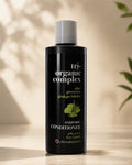 A bottle of Chromastics Tri Organic Complex Extreme Conditioner, featuring a matte black bottle with a white cap, set against a warm beige background with soft leaf shadows.