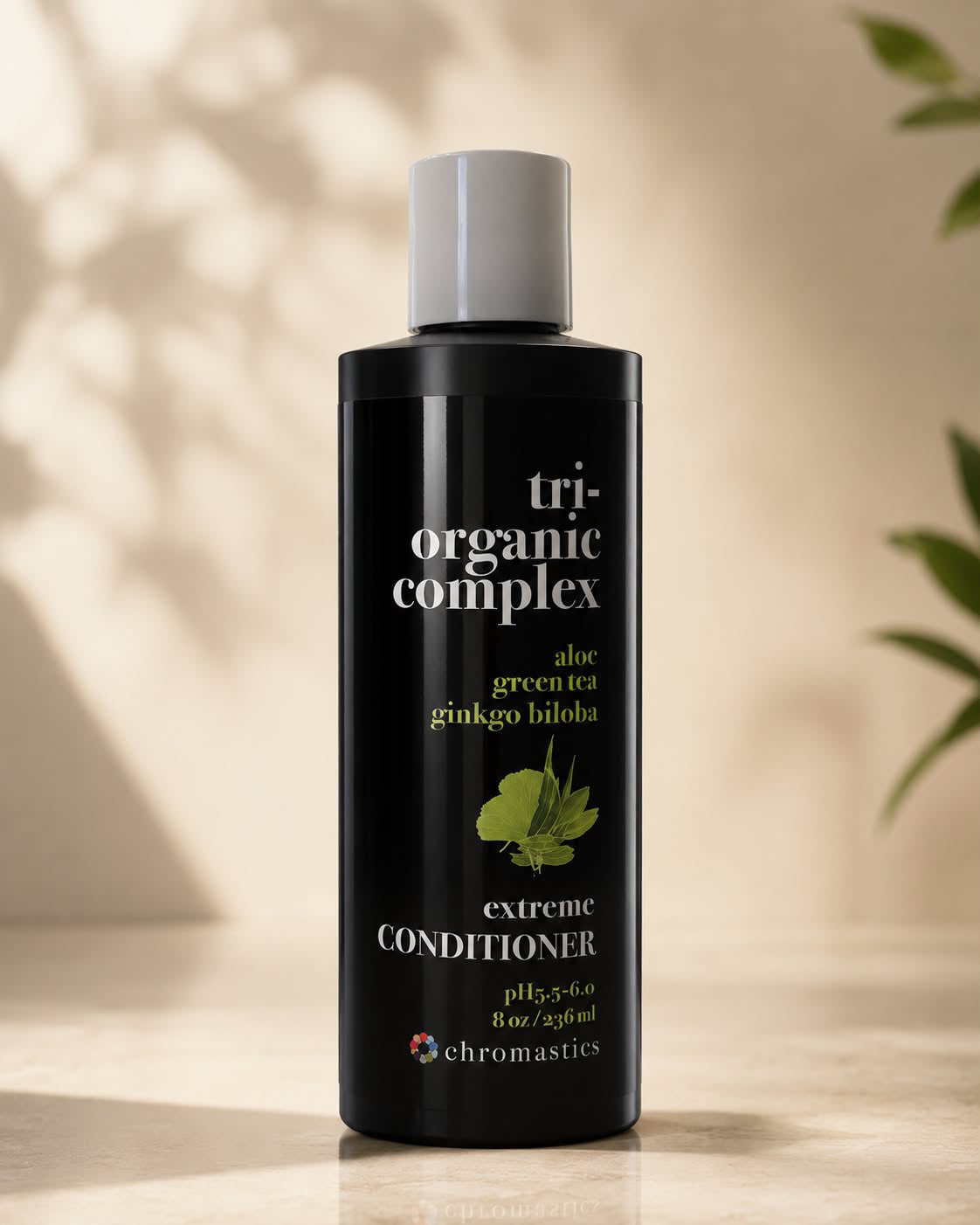 A bottle of Chromastics Tri Organic Complex Extreme Conditioner, featuring a matte black bottle with a white cap, set against a warm beige background with soft leaf shadows.