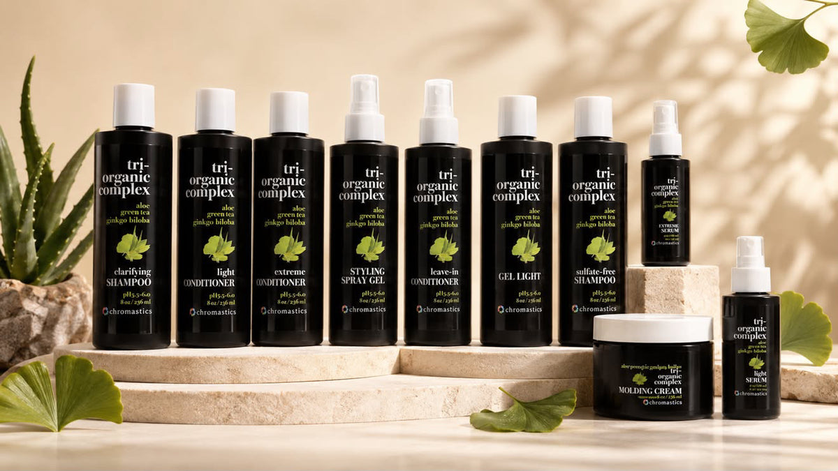 A set of ten tri-organic complex haircare products arranged on beige stone steps with aloe vera and ginkgo leaves. The products include various shampoos, conditioners, sprays, and a scalpeling cream in black bottles with white caps and green/yellow labels.