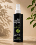 A bottle of Chromatics Tri-Organic Complex Styling Spray Gel, featuring a matte black bottle with a white spray nozzle, set against a warm beige background with soft leaf shadows and green plant leaves on the sides.